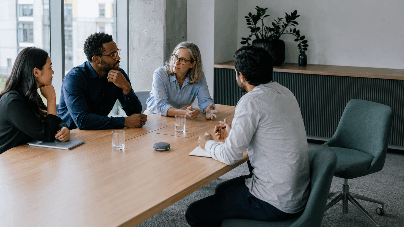 A small meeting group working beside an unoccupied chair and a discreet AI meeting device