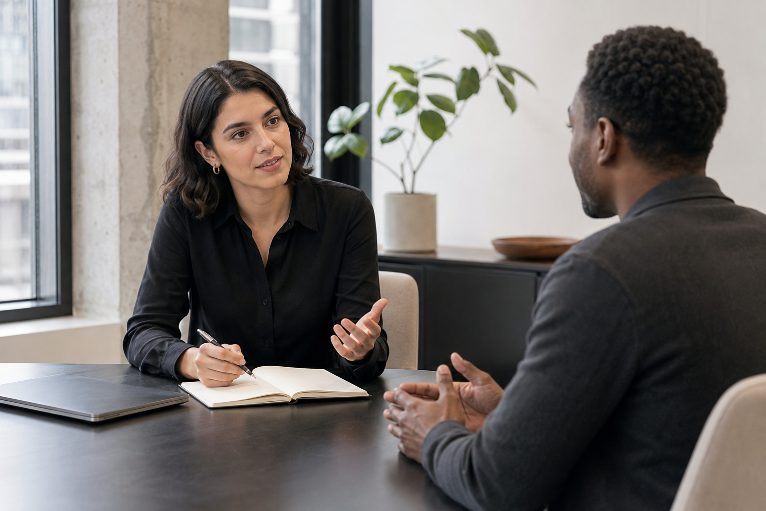 An interviewer and candidate having a focused, natural conversation while a discreet laptop supports note-taking